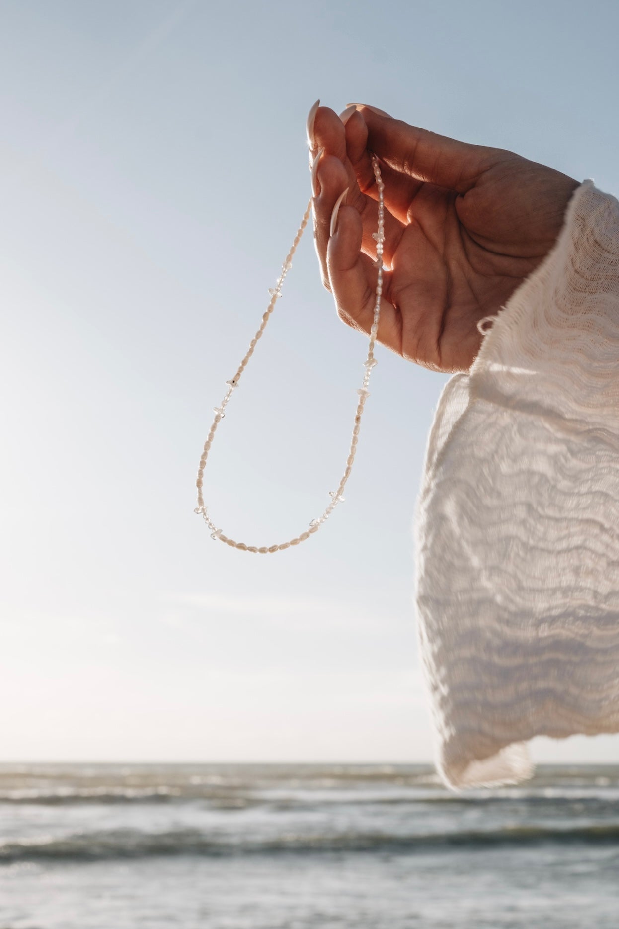 Perlenkette|Choker BLUE MOON Nahaufnahme gehalten in der Luft, mit Meer im Hintergrund