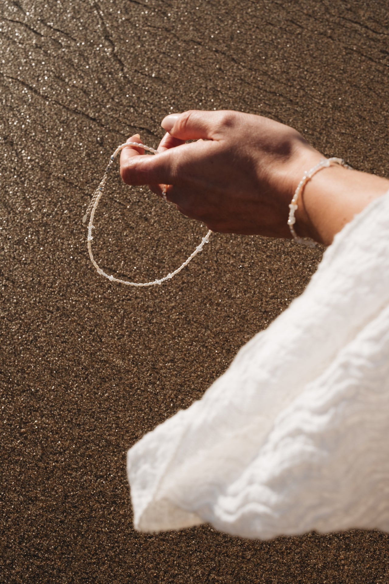 Perlenkette|Choker BLUE MOON in einer Hand gehalten über feuchtem Sand