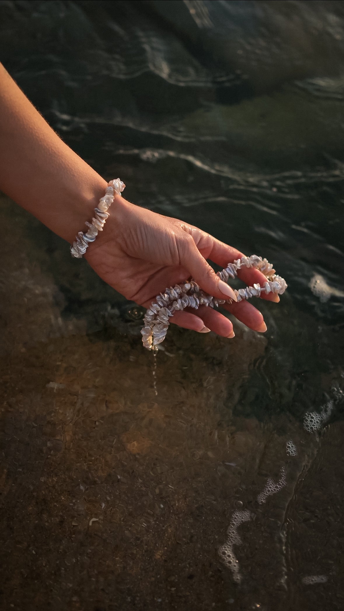 Perlenkette HAWAIIANDREAM und passendes Armband in nasser Hand über der Wasserkante